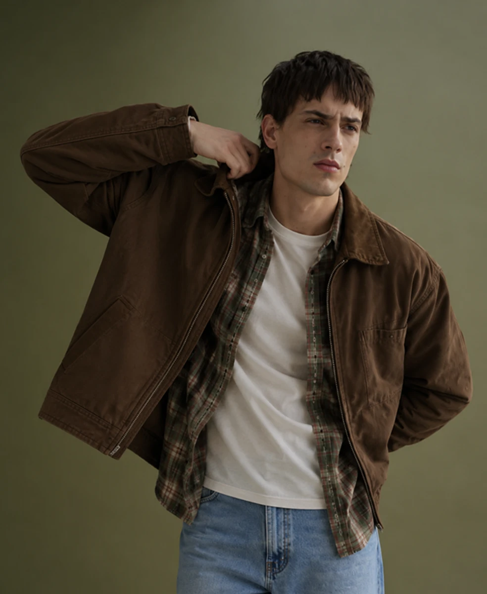 Man in a brown work jacket over a plaid shirt and white tee with light jeans