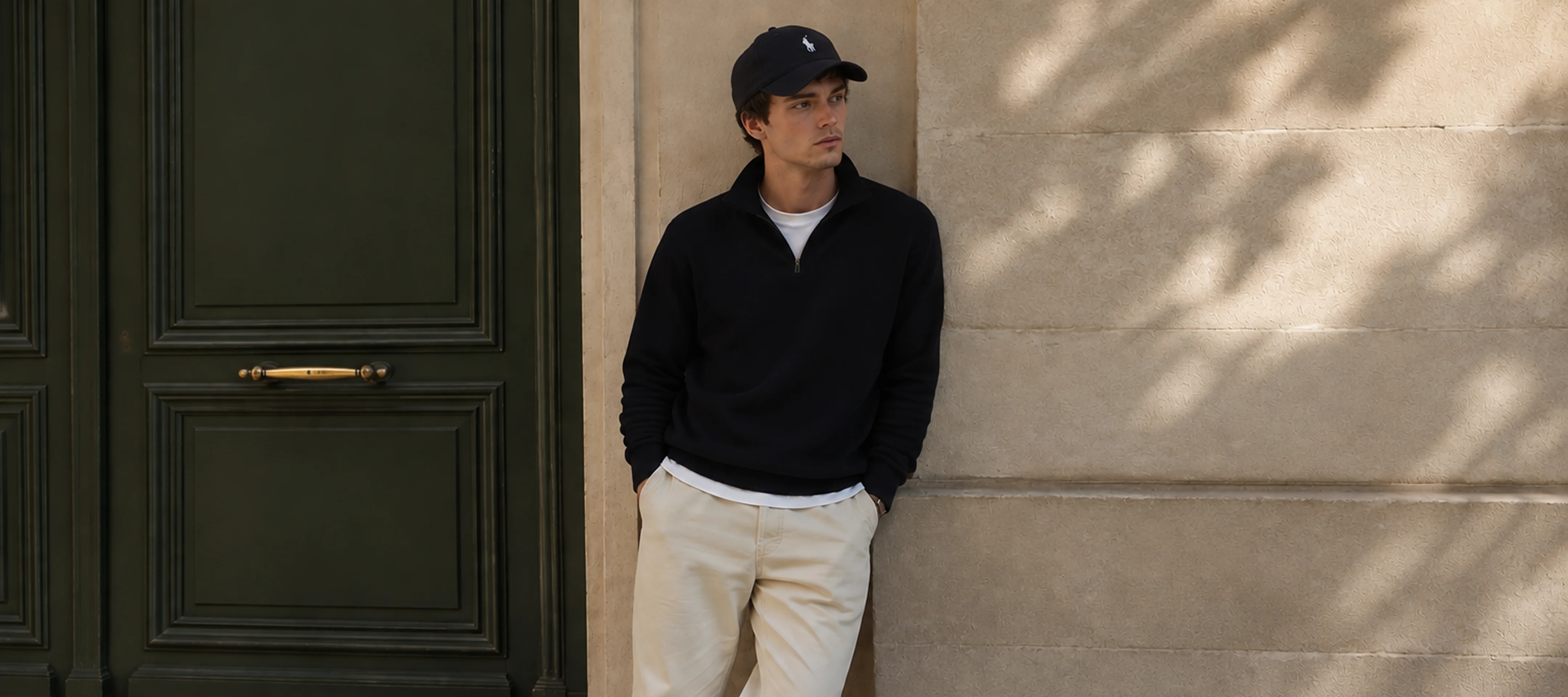 Man leaning against a green doorway in a quarter-zip sweater